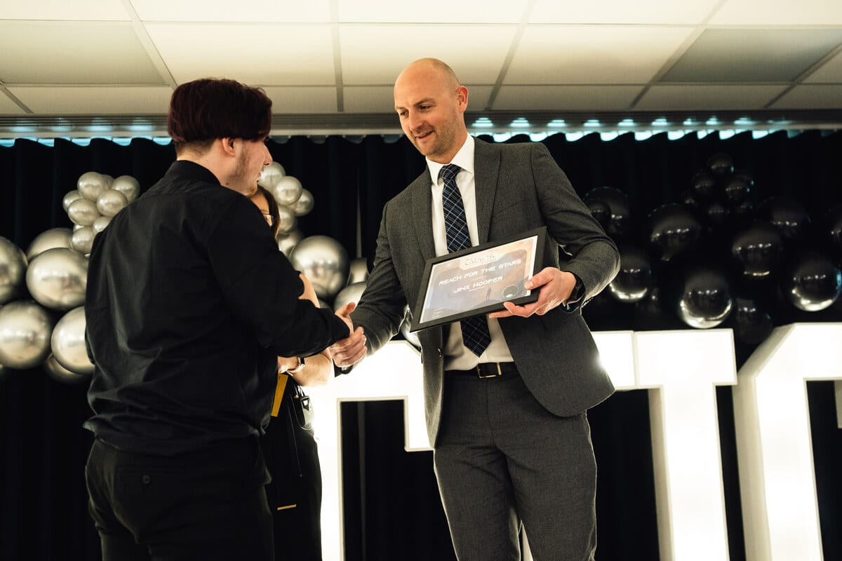 A young person is on stage, shaking hands with a staff member and receiving their award. 