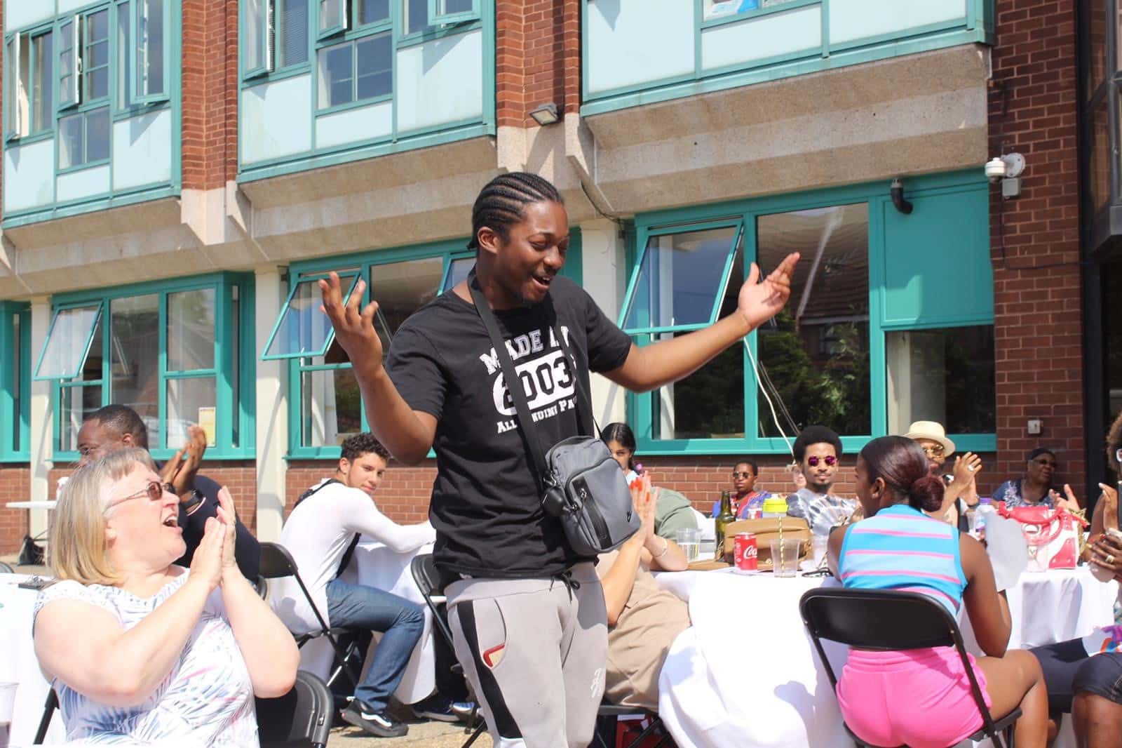 Young people are seated around cabaret tables outside, with a young man dancing in the middle.